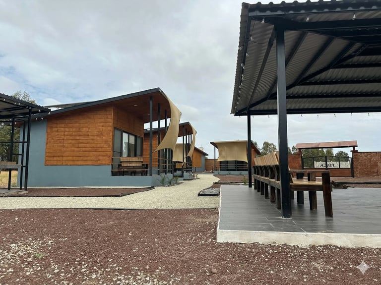 Modern farm buildings with wooden and blue cladding alongside a covered outdoor seating area on gravel grounds