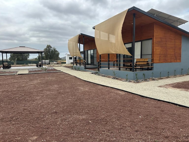 Modern prefab cabin with curved metal roof and brick exterior in a rural setting with gravel grounds and cloudy sky