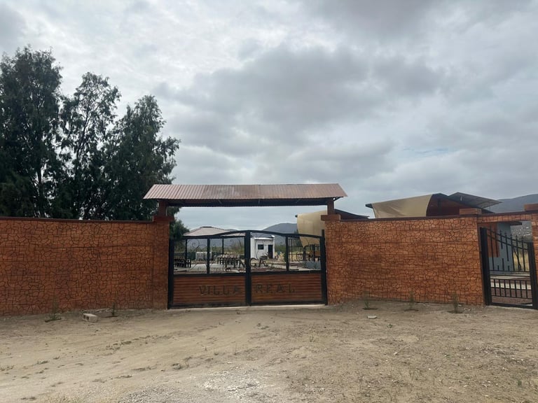 Red brick building with metal gate entrance and windows under cloudy sky with mountains in background